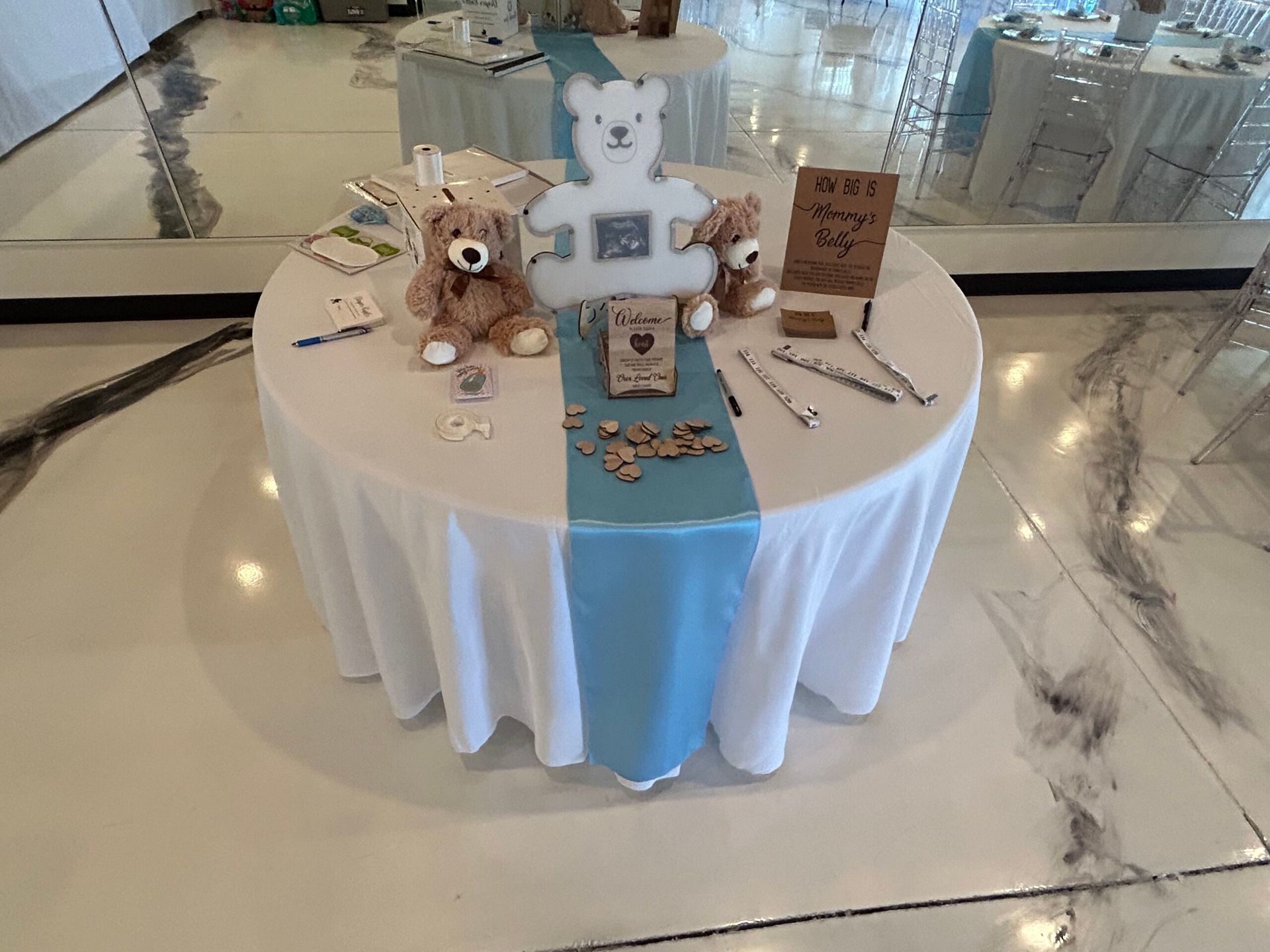 A table with a white table cloth and a blue table runner with teddy bears on it.