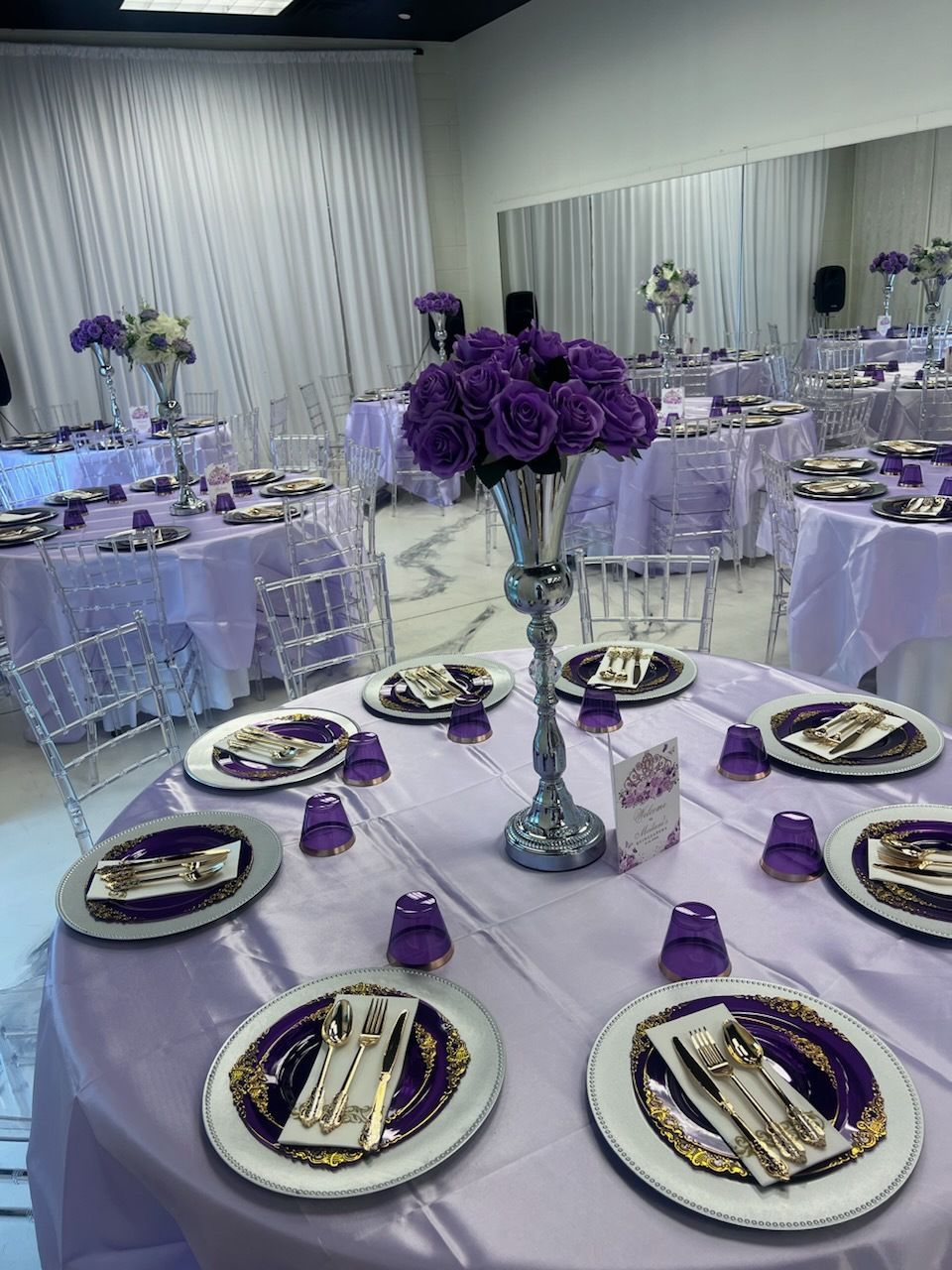 A table set for a wedding reception with purple plates and purple flowers.
