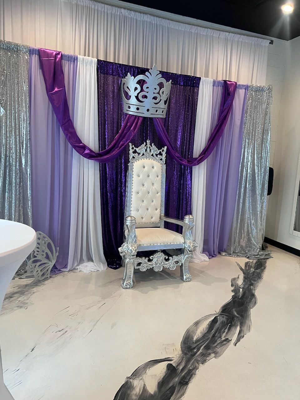 A throne with a crown on it is sitting in front of a purple and white backdrop.