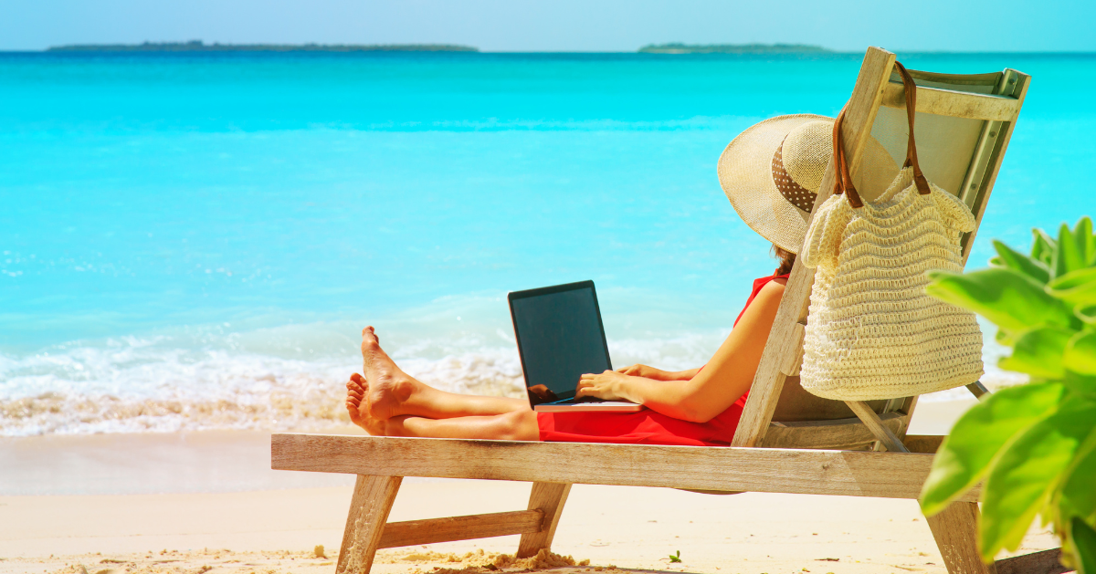 Image of a lady sitting on a sun lounger on the beach using a laptop