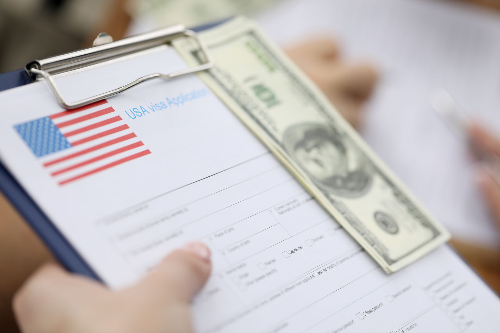 Clipboard with a USA visa application, cash, and hands.