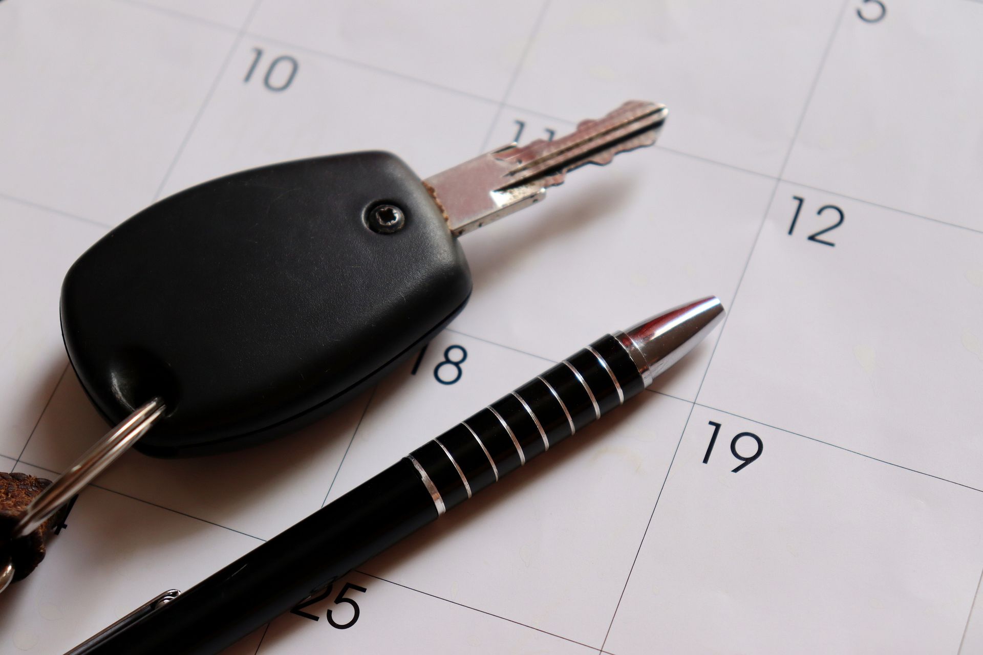 Car keys and pen on a calendar, possibly for scheduling a vehicle appointment.