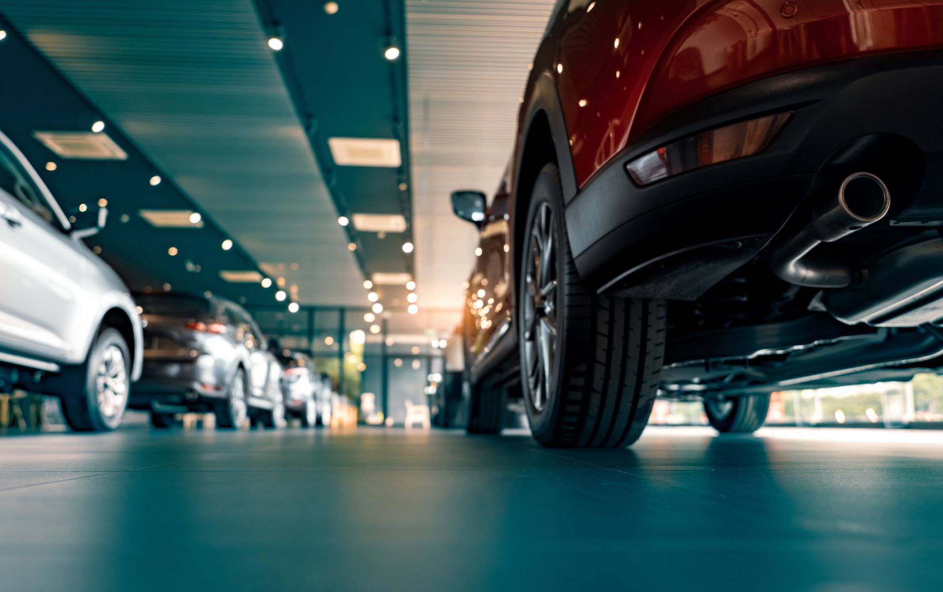 Cars parked inside a showroom, viewed from a low angle, focusing on a red car’s tire.