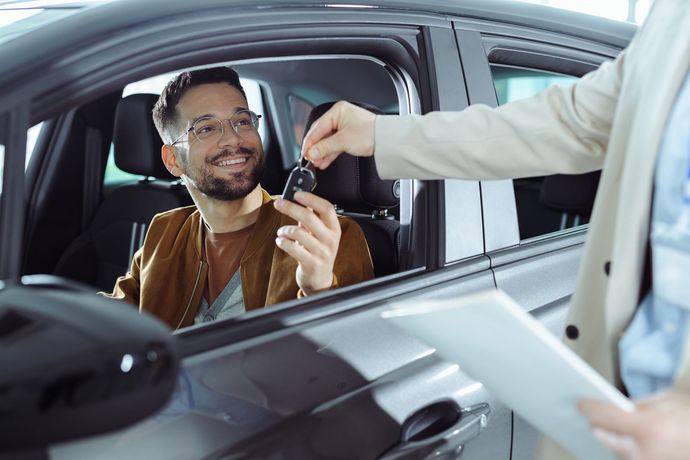 Man in car receiving keys from a person holding documents. Smiling, happy.