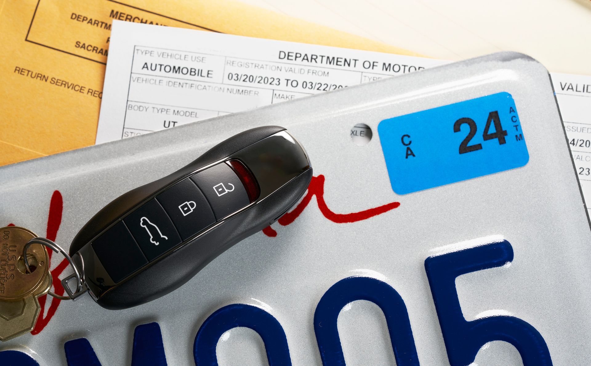 Car key on California license plate with registration sticker and paperwork.