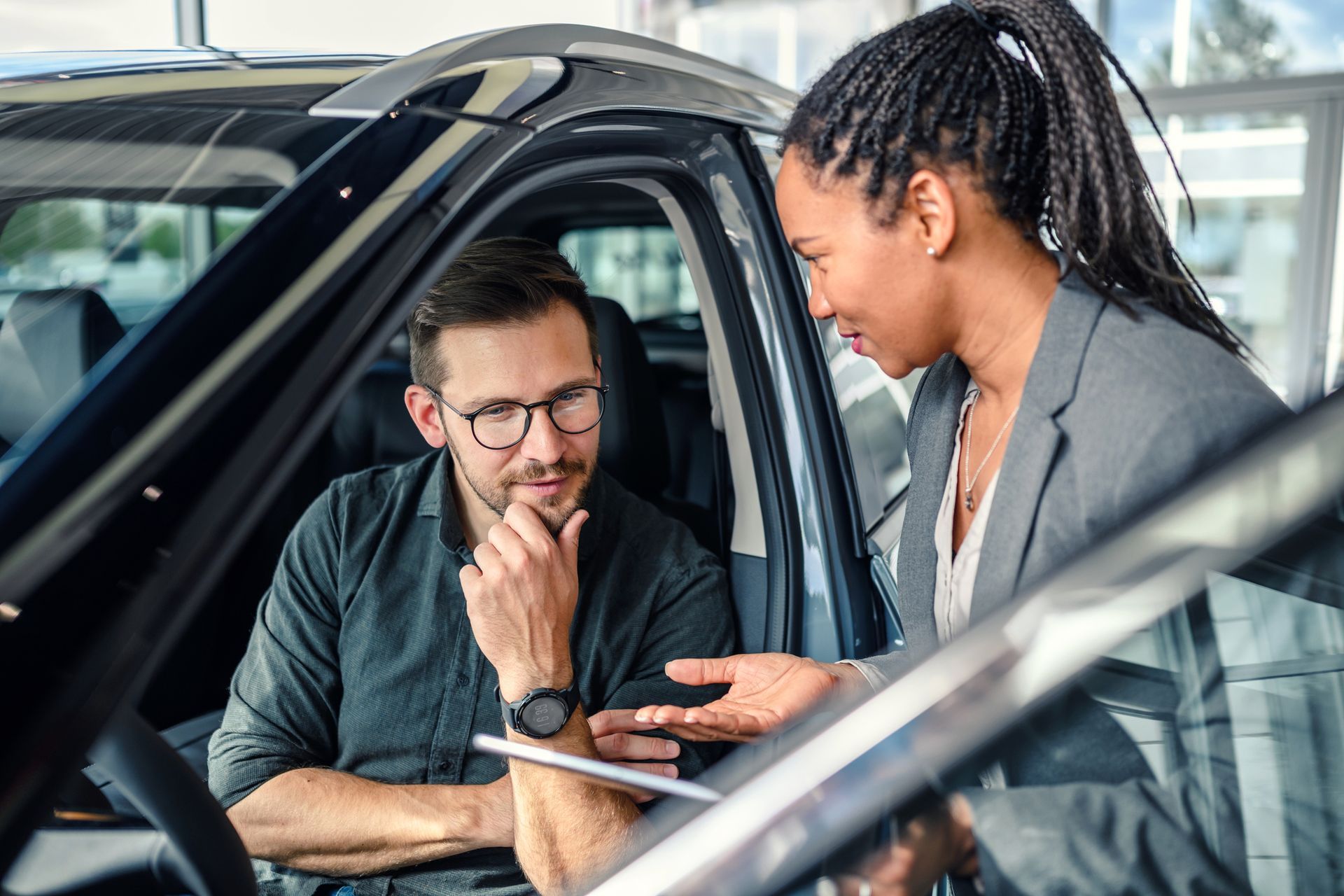 A car salesperson showing a man a vehicle's interior. They are in a car dealership.
