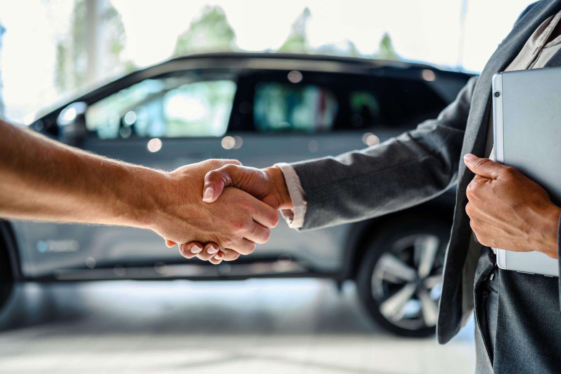 Handshake between a customer and car salesperson in a car dealership, with a car visible in the background.