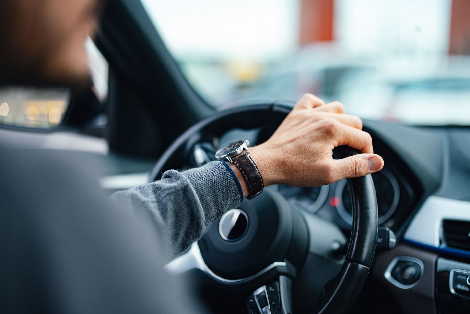 Person driving a car, holding the steering wheel with one hand.