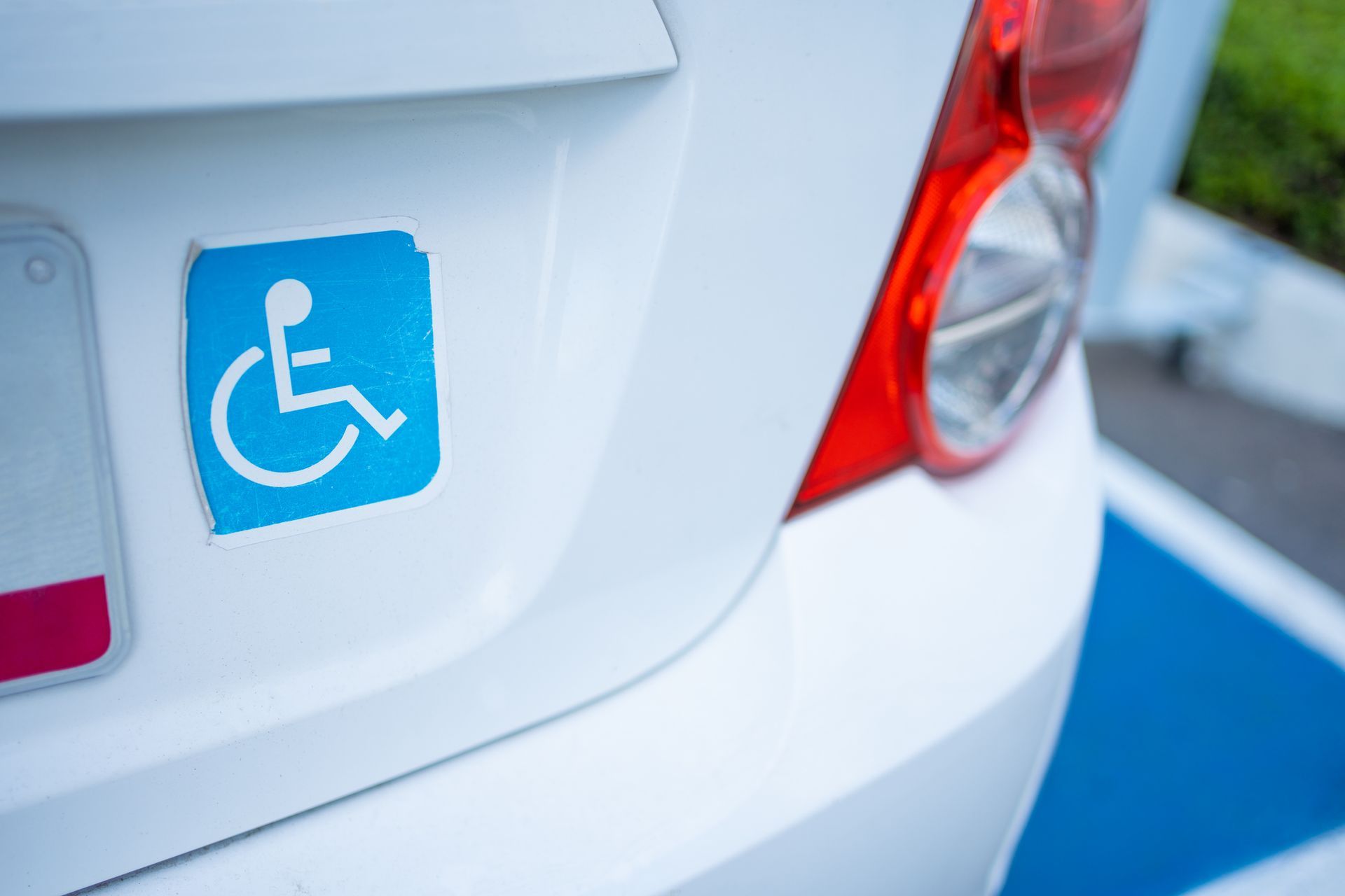 White car with a blue handicapped parking sticker on the trunk near the tail light.