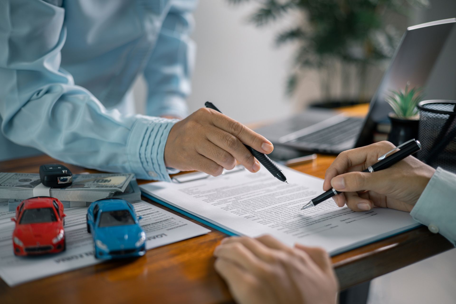 Two people signing car insurance documents; toy cars and cash on desk. Two people signing car insurance documents; toy cars and cash on desk.