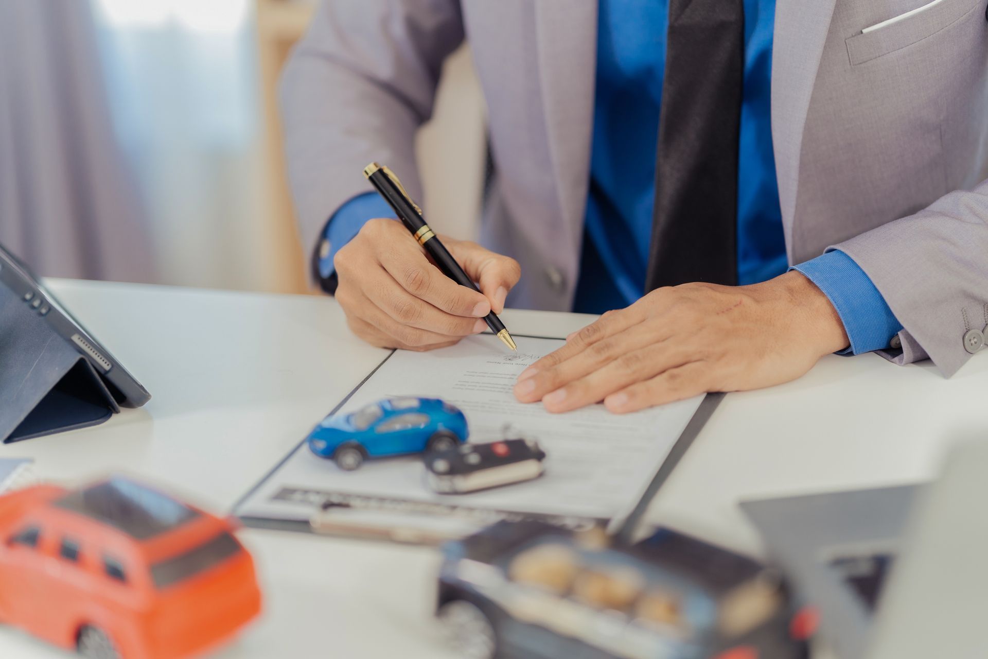 Man in suit signing paperwork with car models on a desk. Man in suit signing paperwork with car models on a desk.