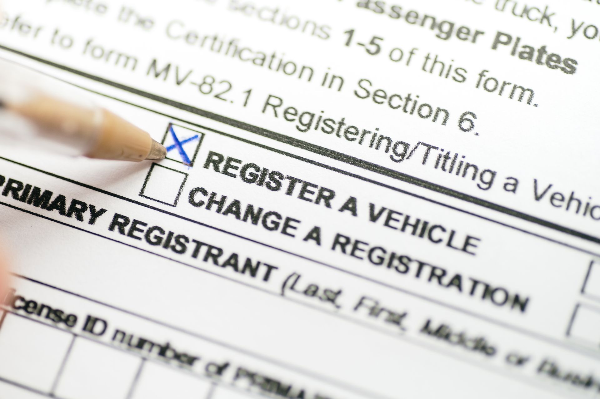 A hand filling out a vehicle registration form, checking the box for 