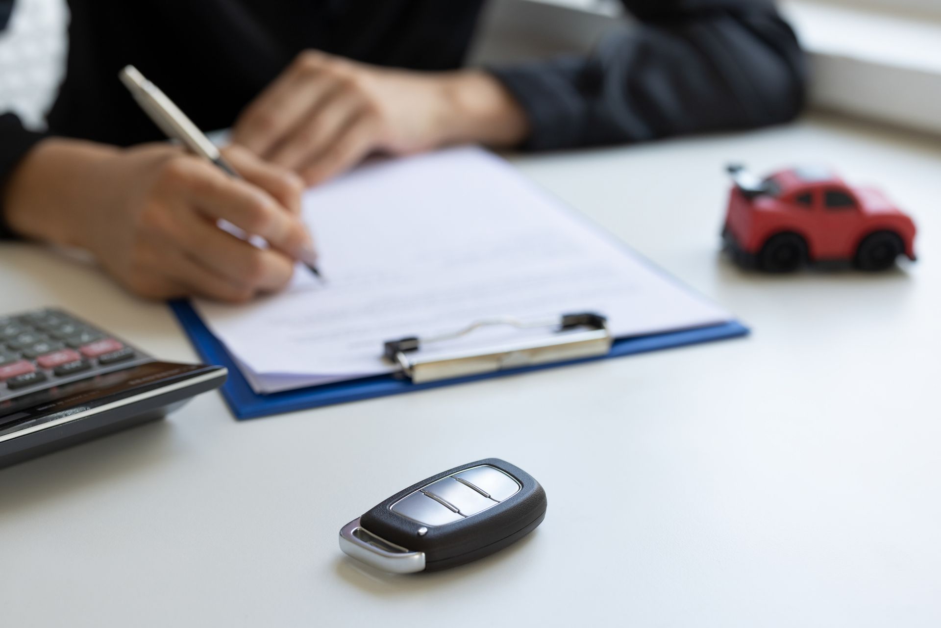 Person signing car paperwork, car key and toy car on desk. Person signing car paperwork, car key and toy car on desk.