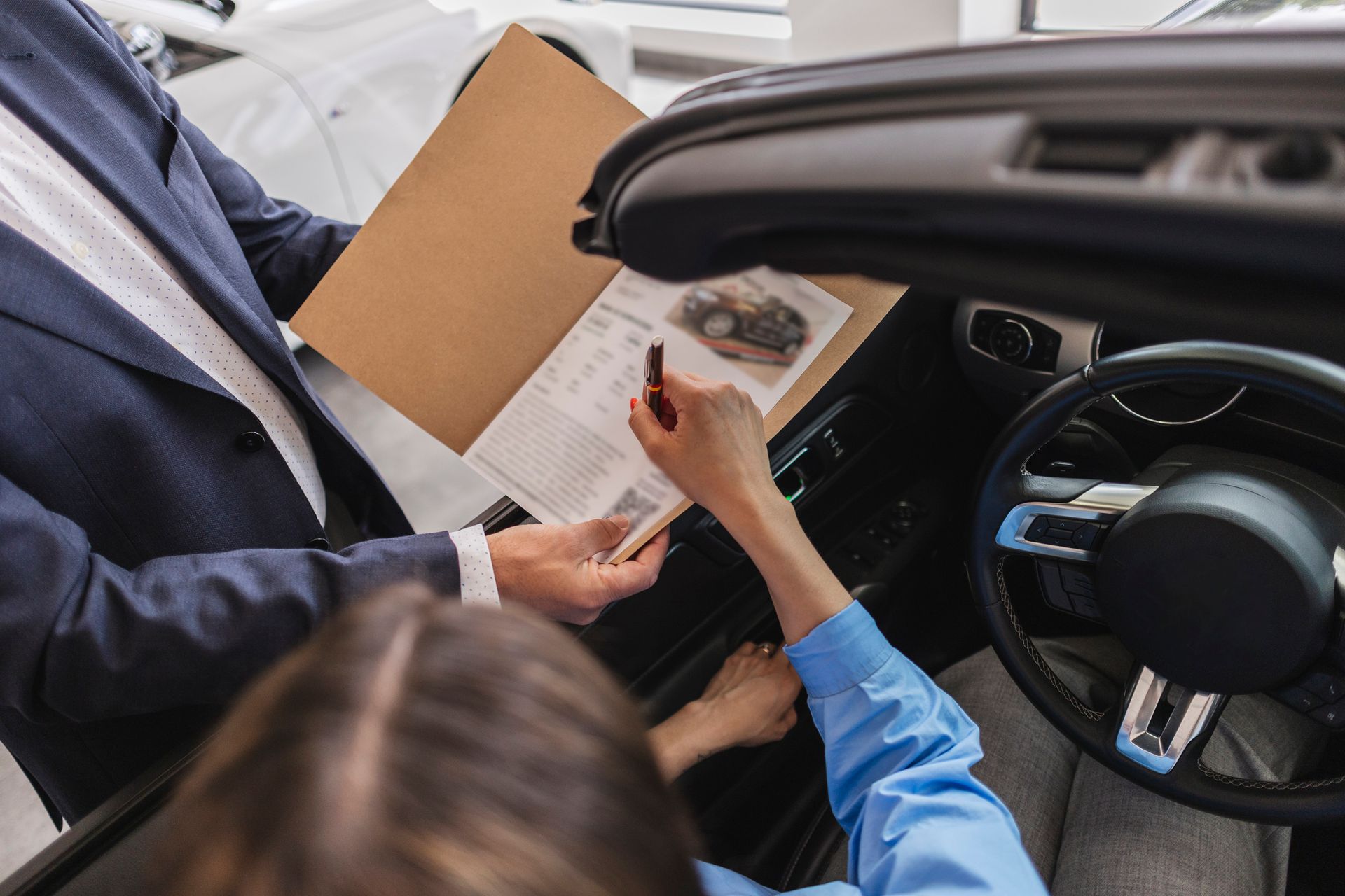 Person in car signing papers with a salesperson; car dealership setting.
