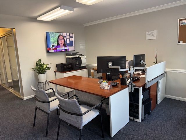 Office space with a desk, chairs, computers, TV, and printer.