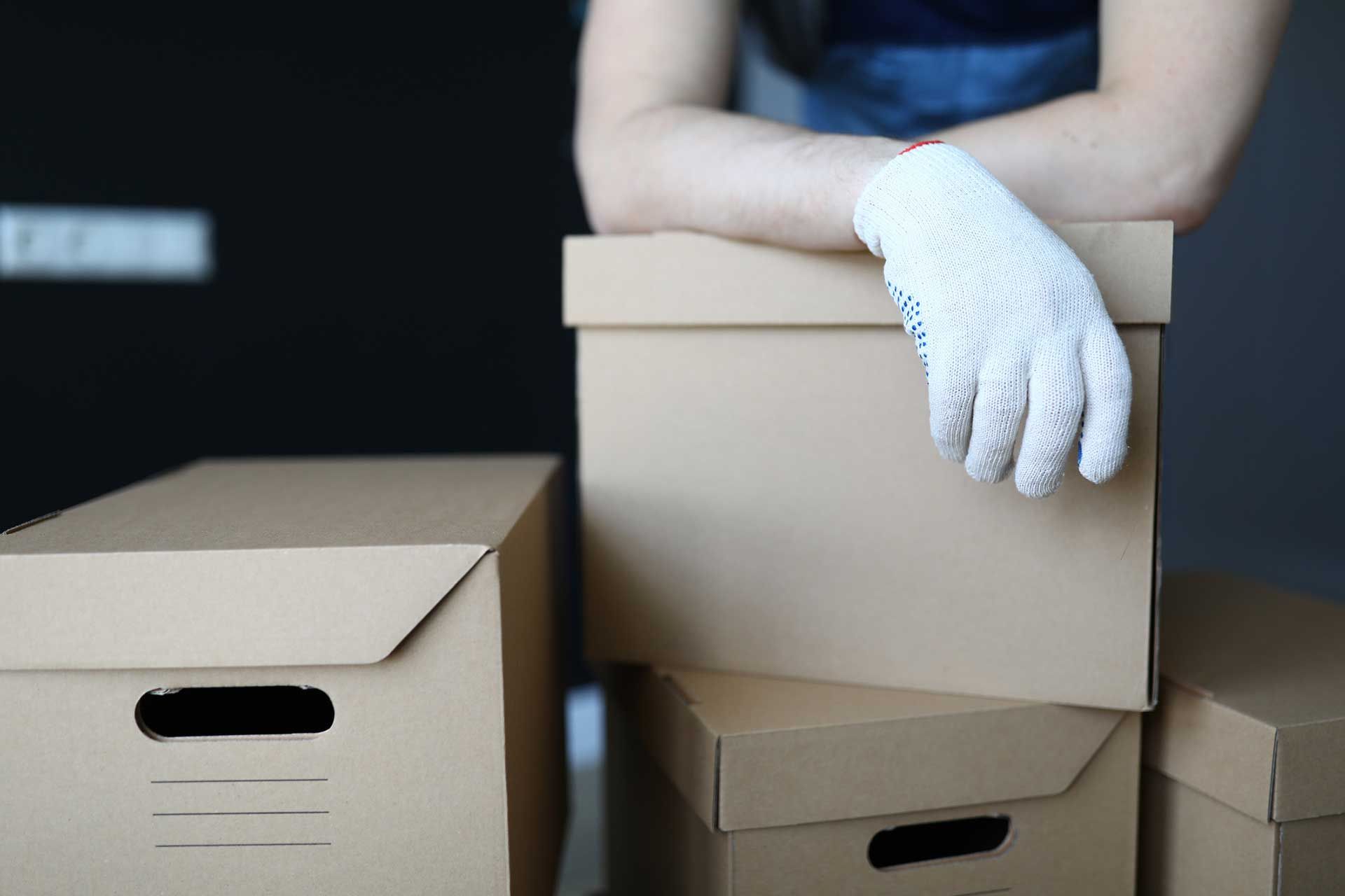 person wearing gloves standing behind and leaning against a stack of moving boxes