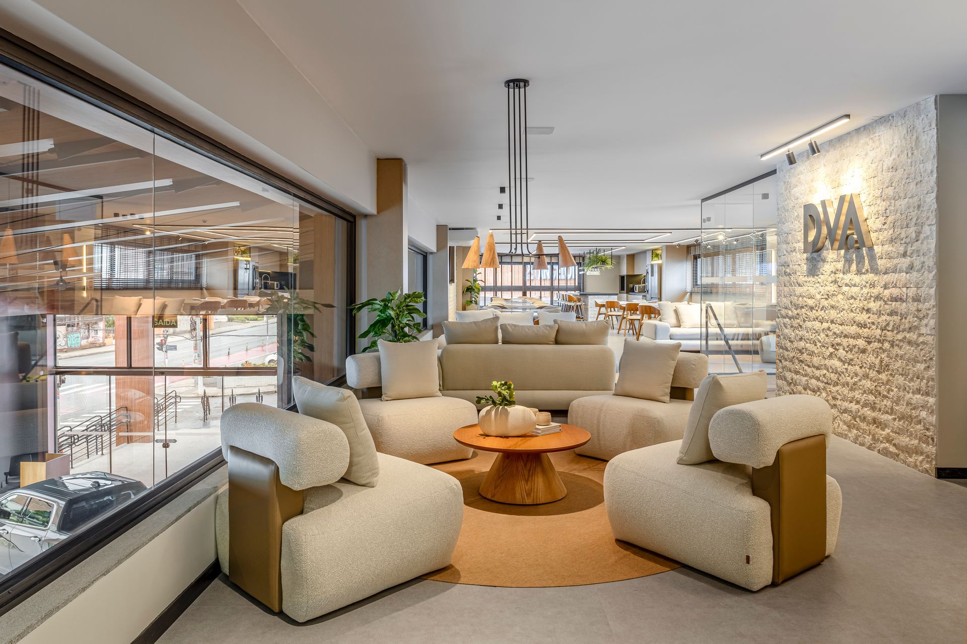 Sala de estar com sofá creme, cadeiras e mesa redonda laranja. Parede de tijolos à direita.