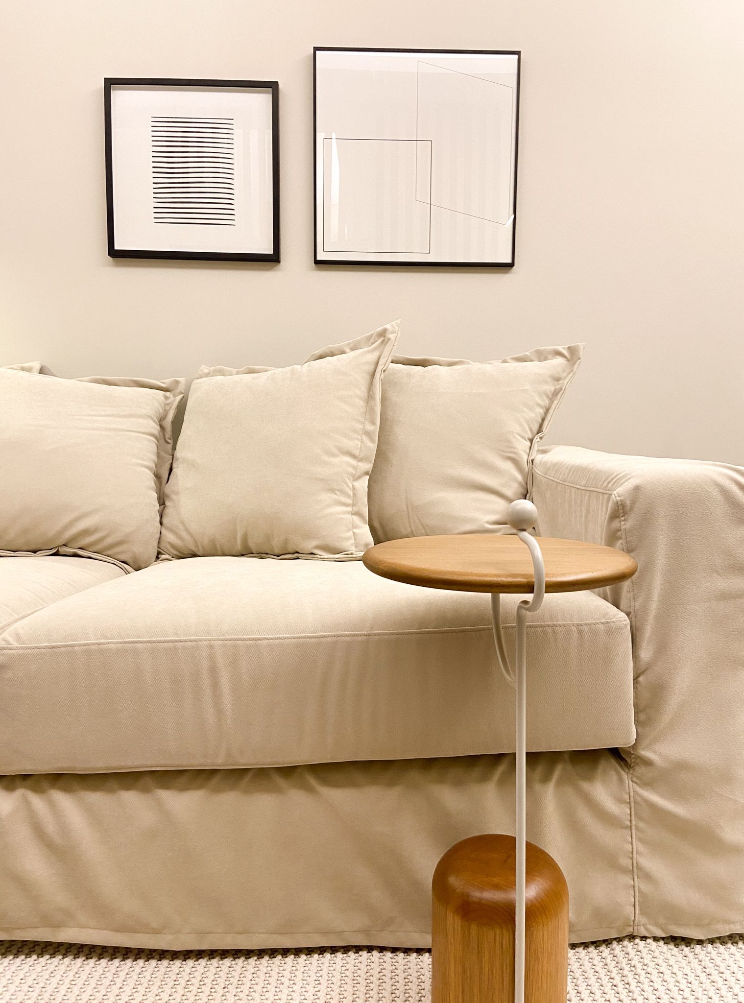 Sofá bege com almofadas franjadas, mesa lateral e arte abstrata em uma parede de cor clara.