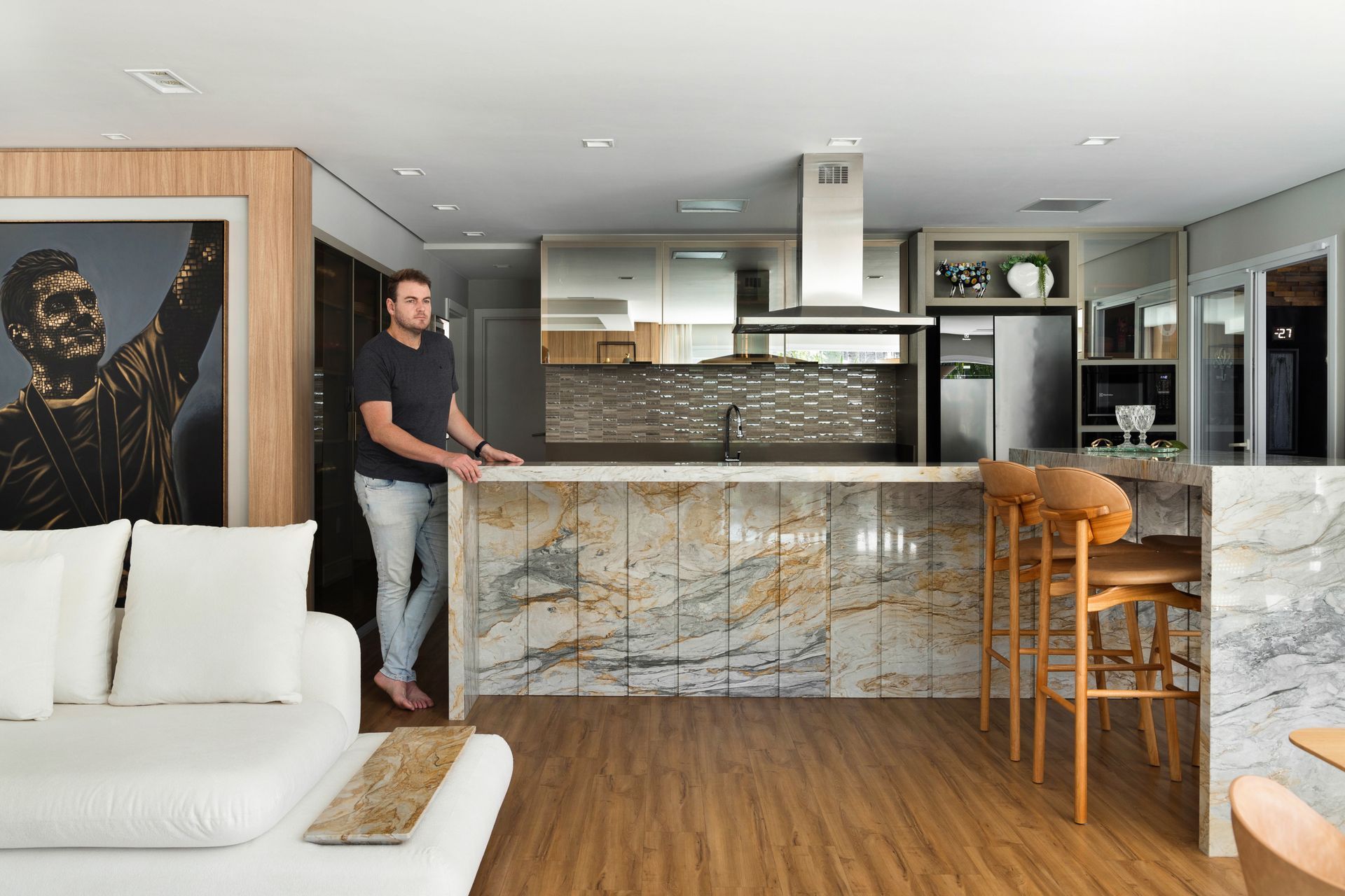 Um homem está de pé em uma sala de estar ao lado de um sofá e uma cozinha.