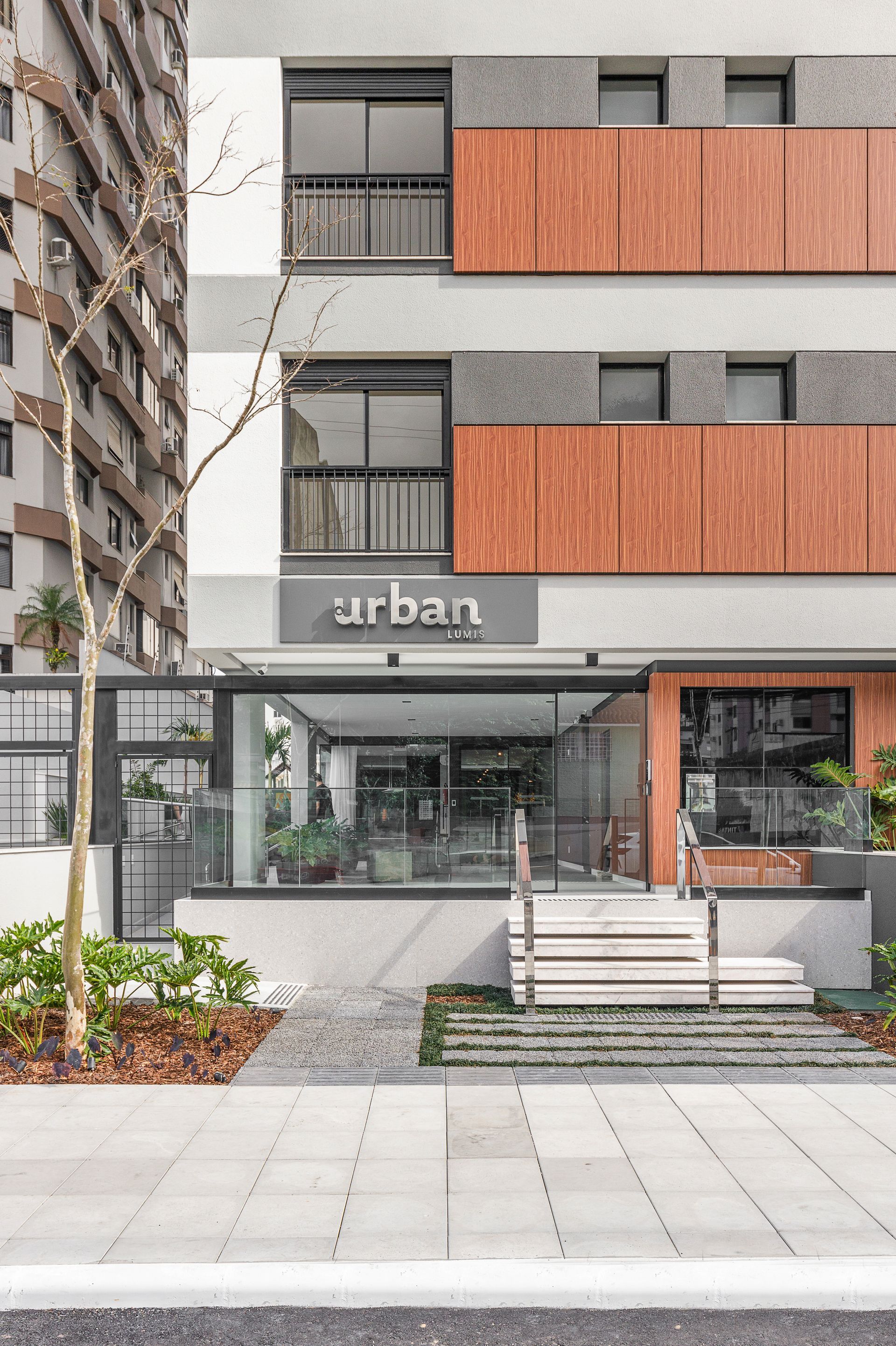 Exterior de edifício de apartamentos urbanos com entrada de vidro, painéis de madeira e placa.