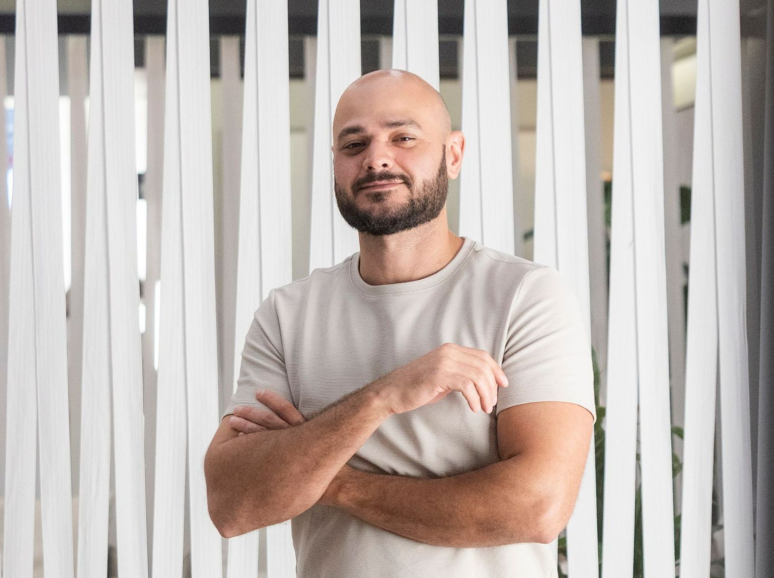 Homem careca, com barba, braços cruzados, camisa clara. Fundo vertical branco.