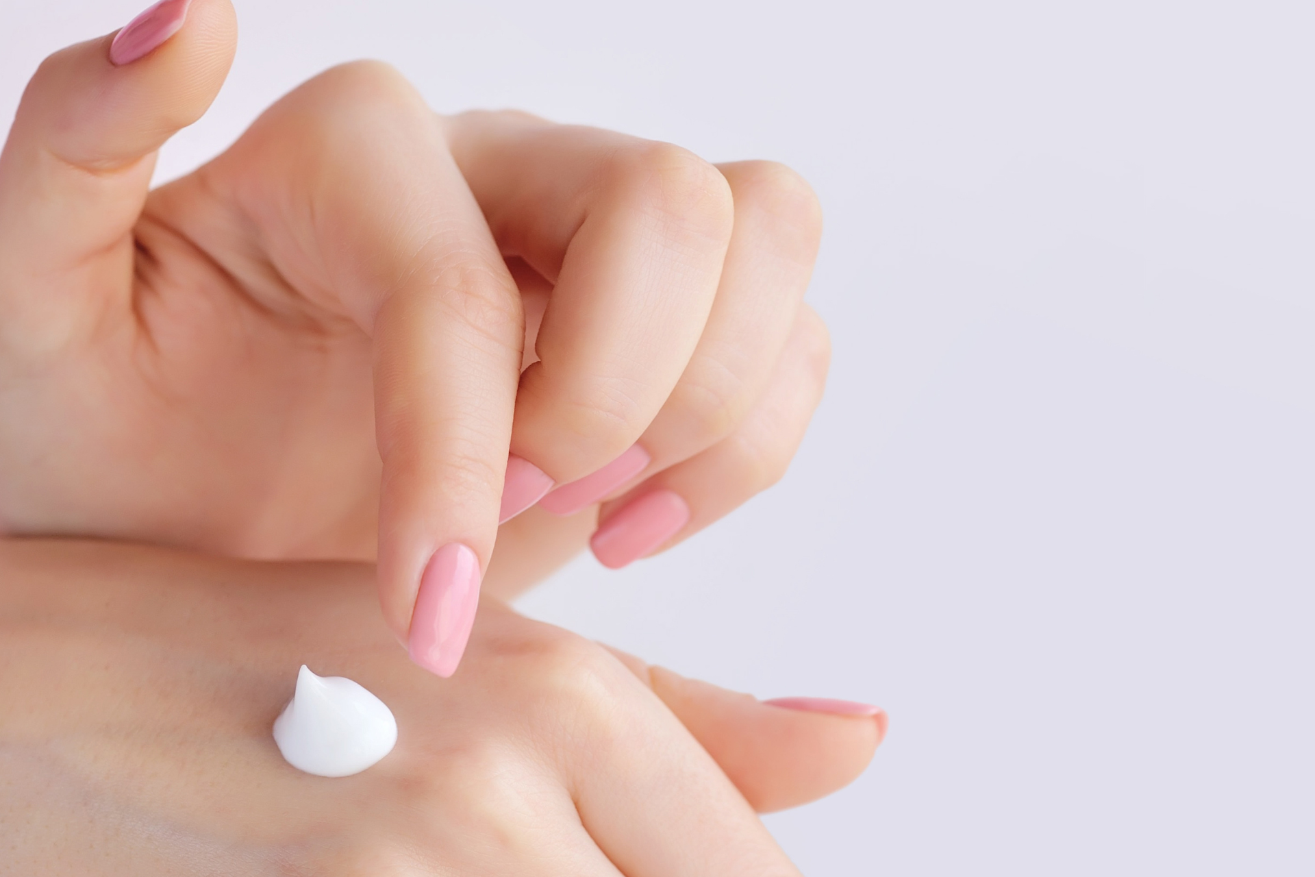 Mani con smalto rosa chiaro, su cui è stata applicata una noce di crema bianca.