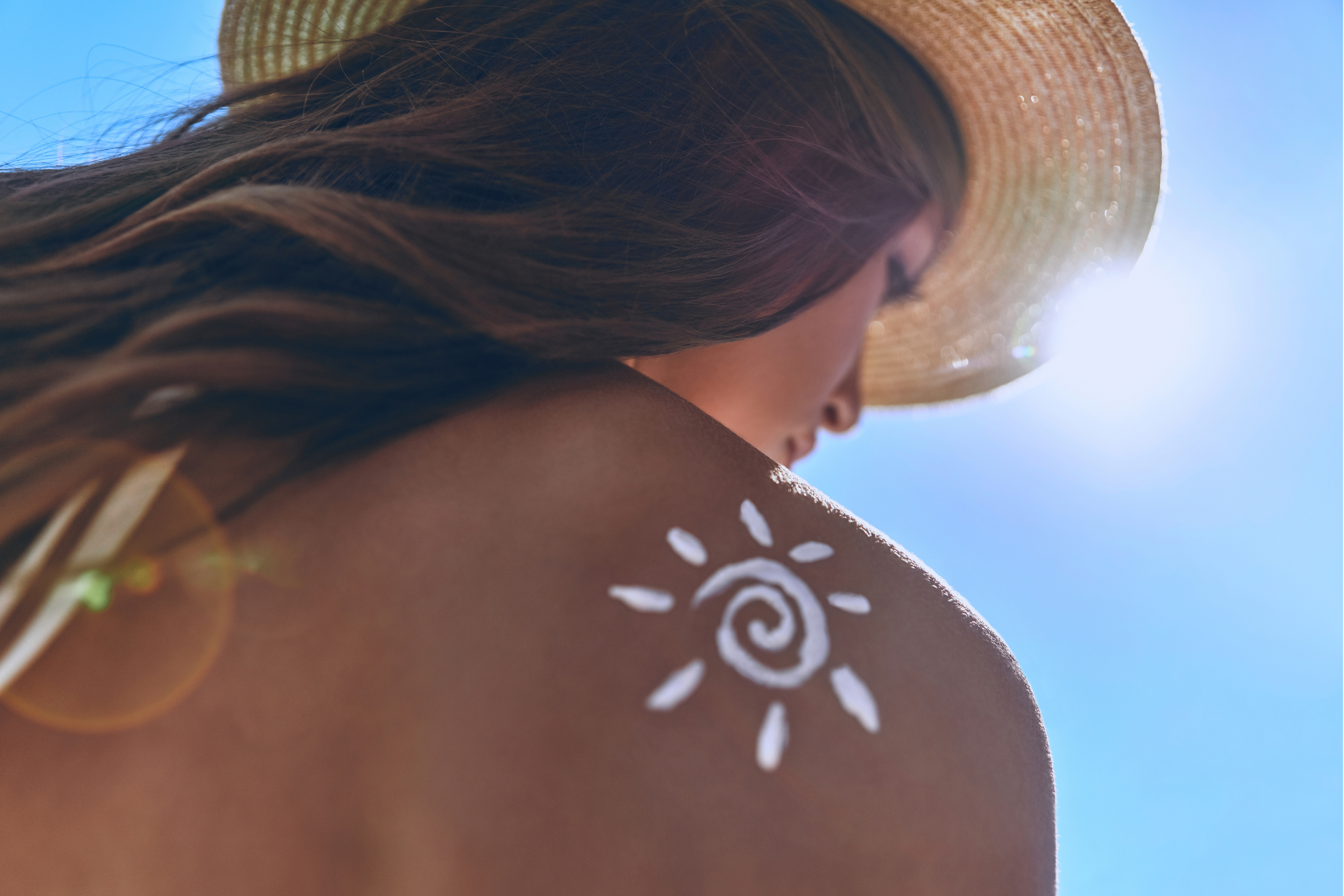 Donna con crema solare a forma di sole sulla spalla, che indossa un cappello di paglina