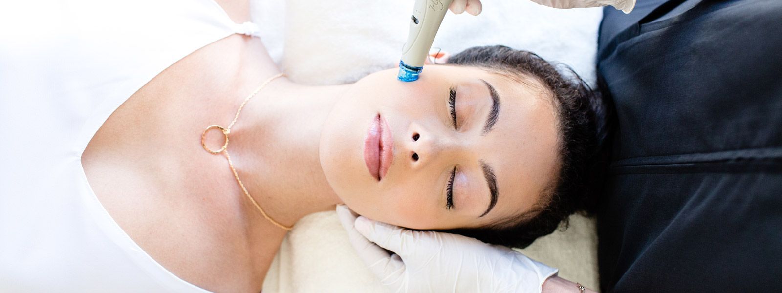 Donna che riceve un trattamento viso, con gli occhi chiusi. Un dispositivo tenuto da mani guantate le tocca il viso.