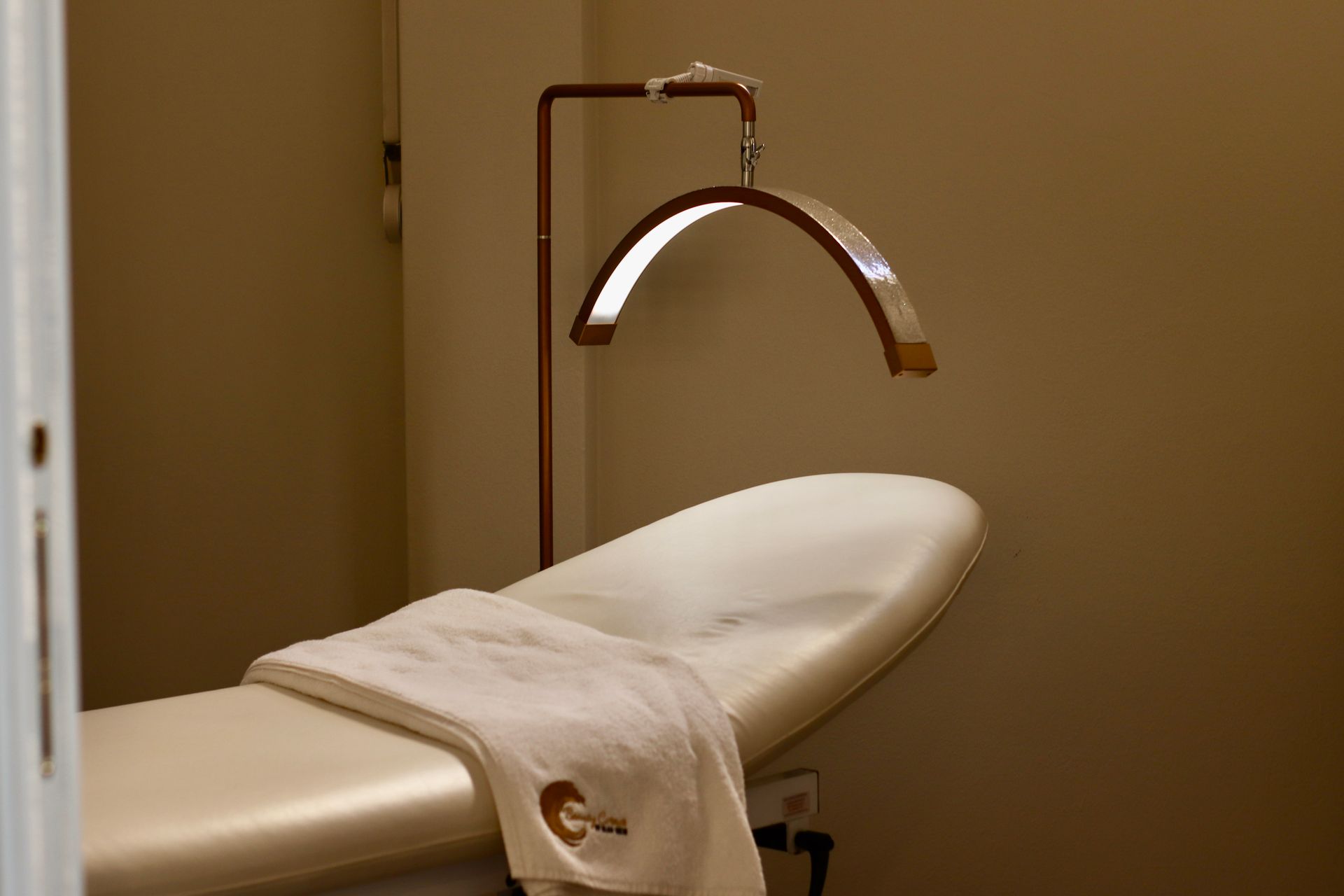 Sala per trattamenti spa con lettino per massaggi, lampada a sospensione e asciugamano piegato.