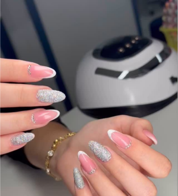 Mani con nail art glitterata rosa e argento; sullo sfondo una luce UV bianca.