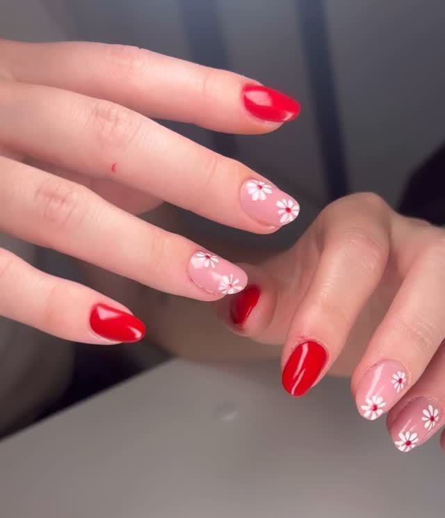 Mani con unghie rosse e decorate con margherite. Le unghie sono ovali.