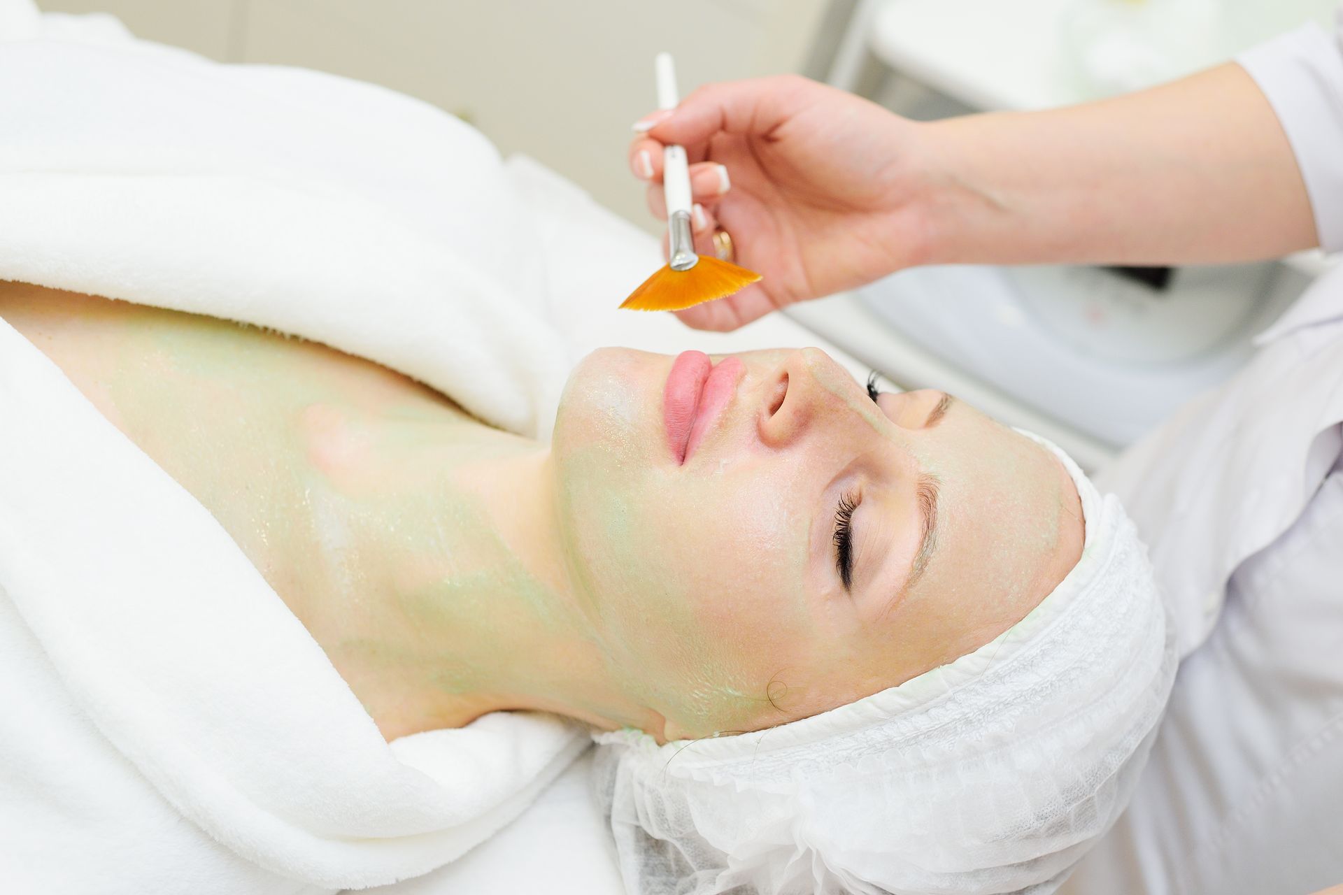 Donna che riceve un trattamento viso in una spa. L'estetista le applica una maschera verde.