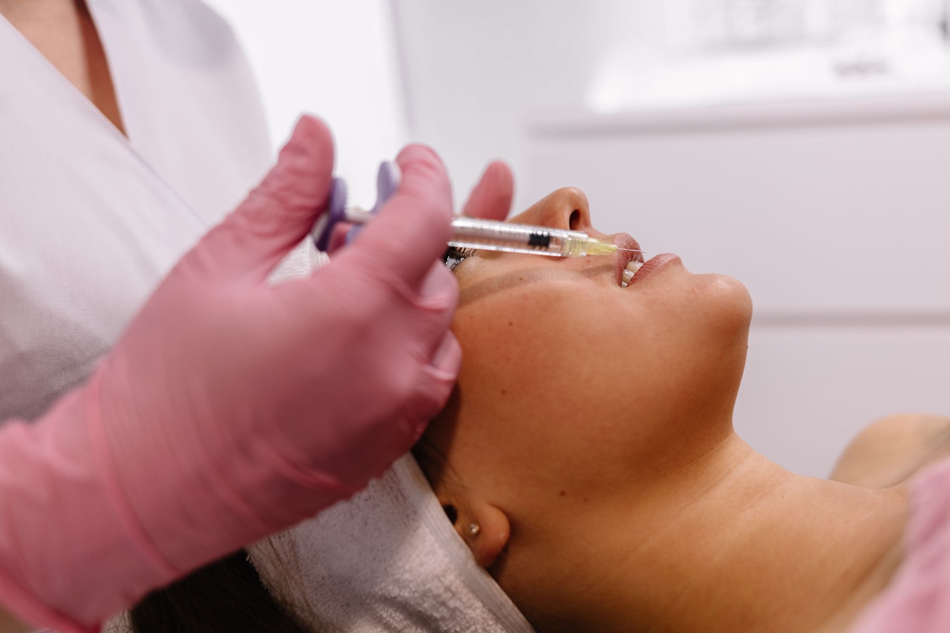 Donna che riceve un'iniezione facciale vicino al naso, somministrata da qualcuno che indossa guanti rosa.