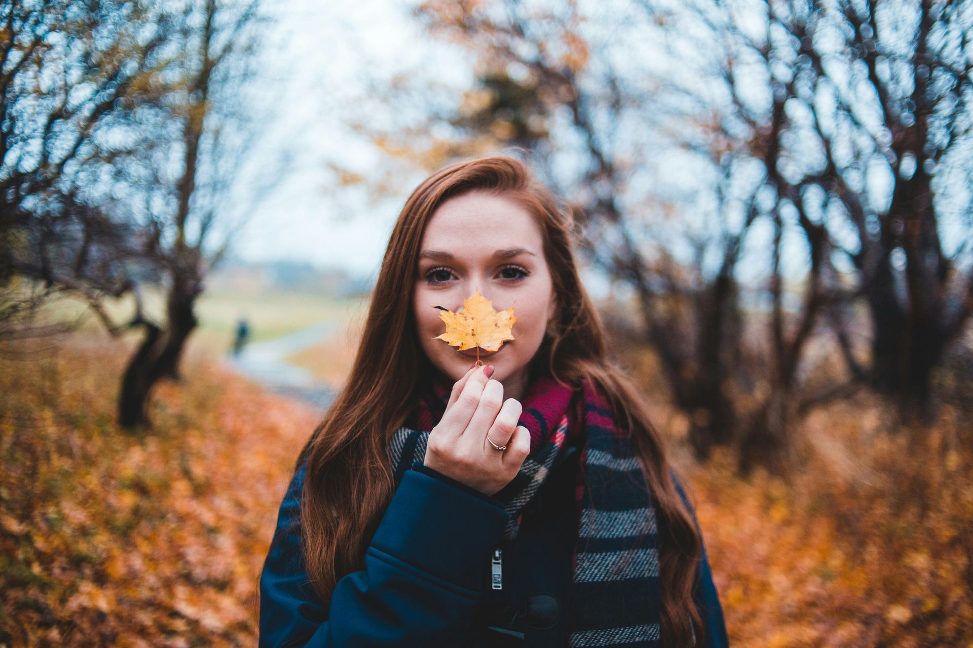 Woman holding a yellow leaf to her nose, standing in a path surrounded by fall foliage.