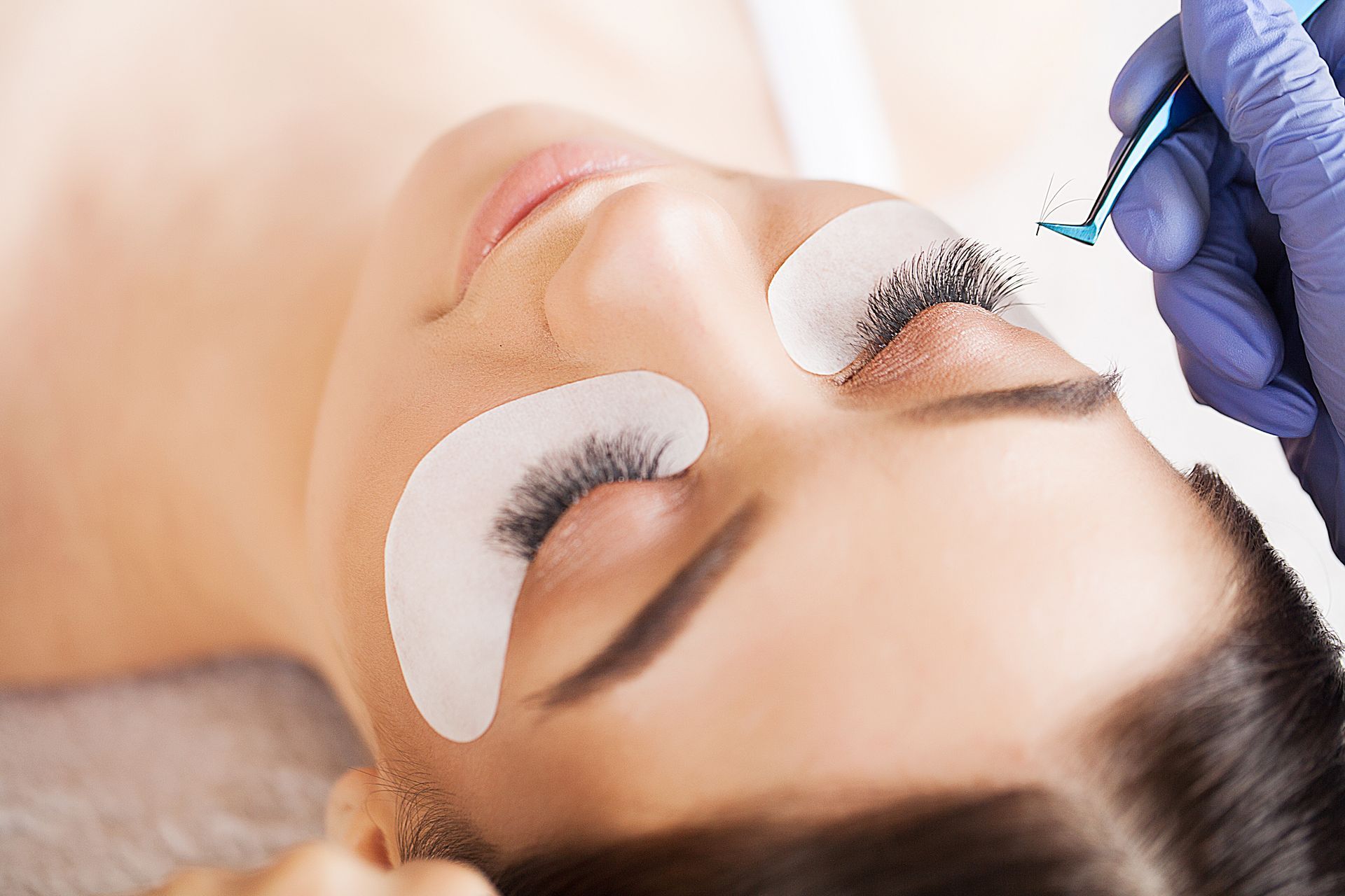 Donna che si fa applicare le extension alle ciglia; sdraiata con dei cerotti sugli occhi.