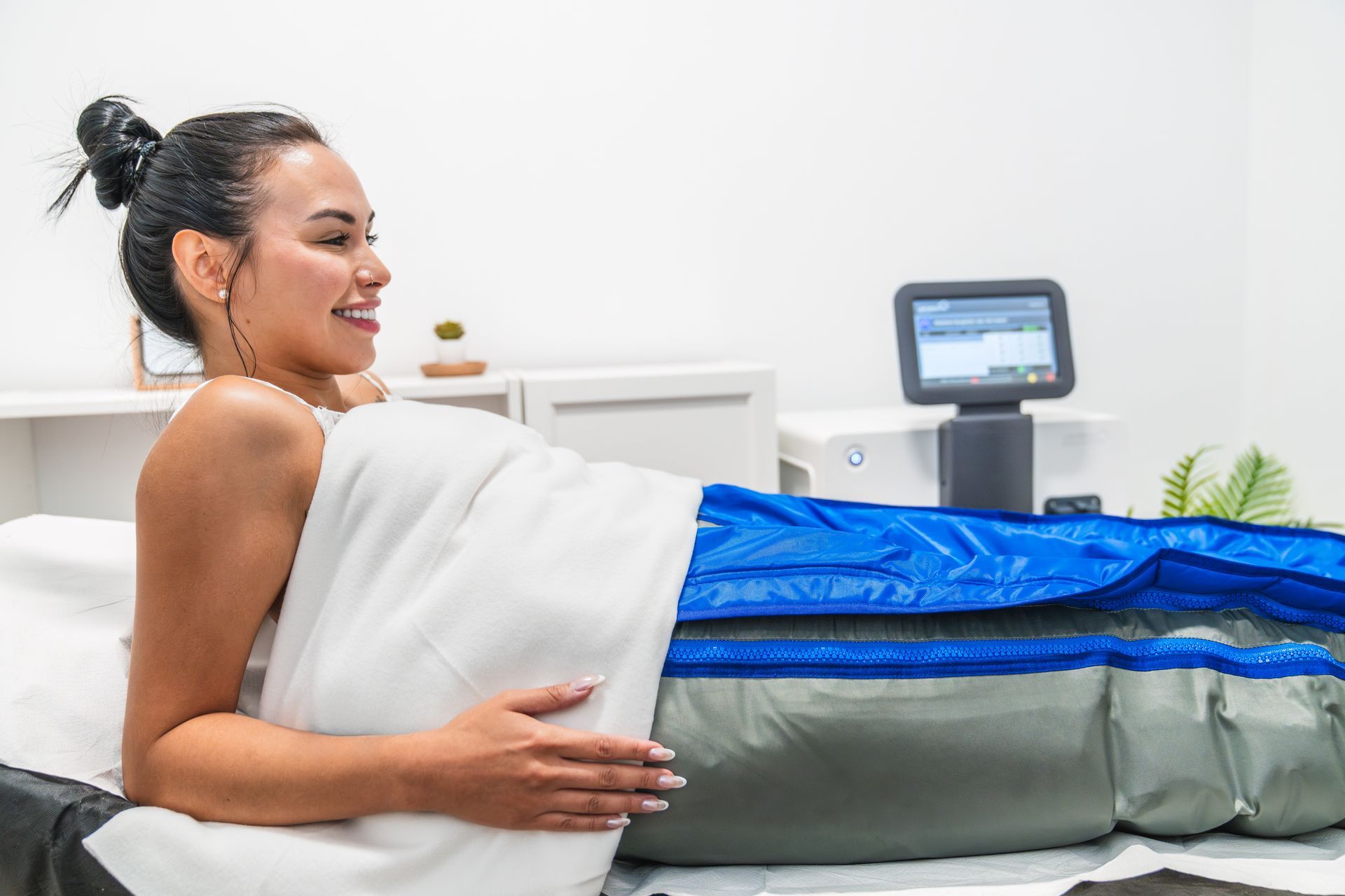 Donna sorridente che riceve un trattamento di body wrap in una spa. Sono visibili il dispositivo azzurro e grigio.
