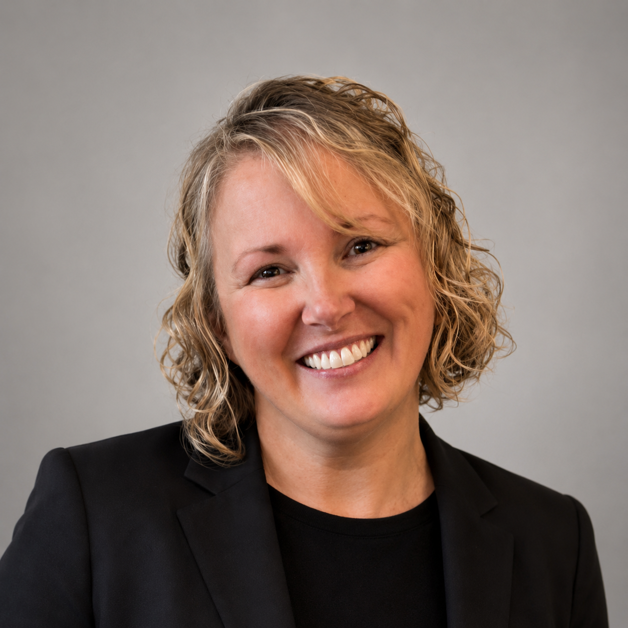 Smiling woman in a black blazer against a gray background
