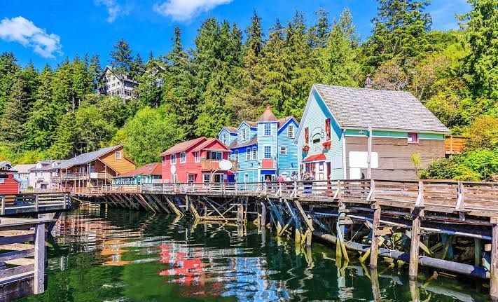 Colorful waterfront houses on a wooden pier beside calm harbor water and forested hillside