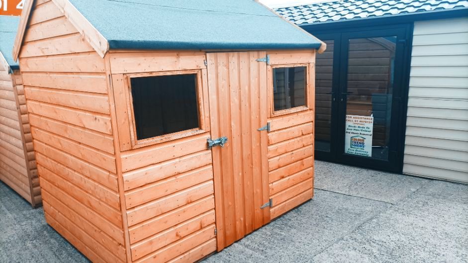 A wooden shed with a green roof and two windows