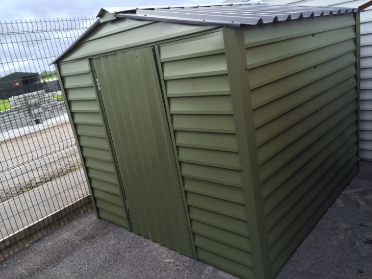 A green shed with a black roof is sitting on the ground