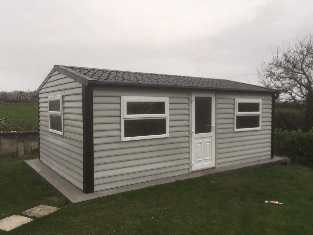 A small white house with a black roof is sitting in the middle of a lush green field.