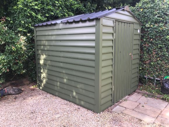 A green shed with a black roof is sitting on gravel in a backyard.