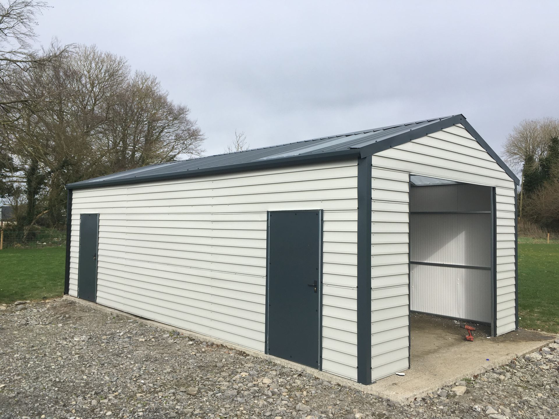 A white garage with a black roof is sitting in the middle of a gravel road.
