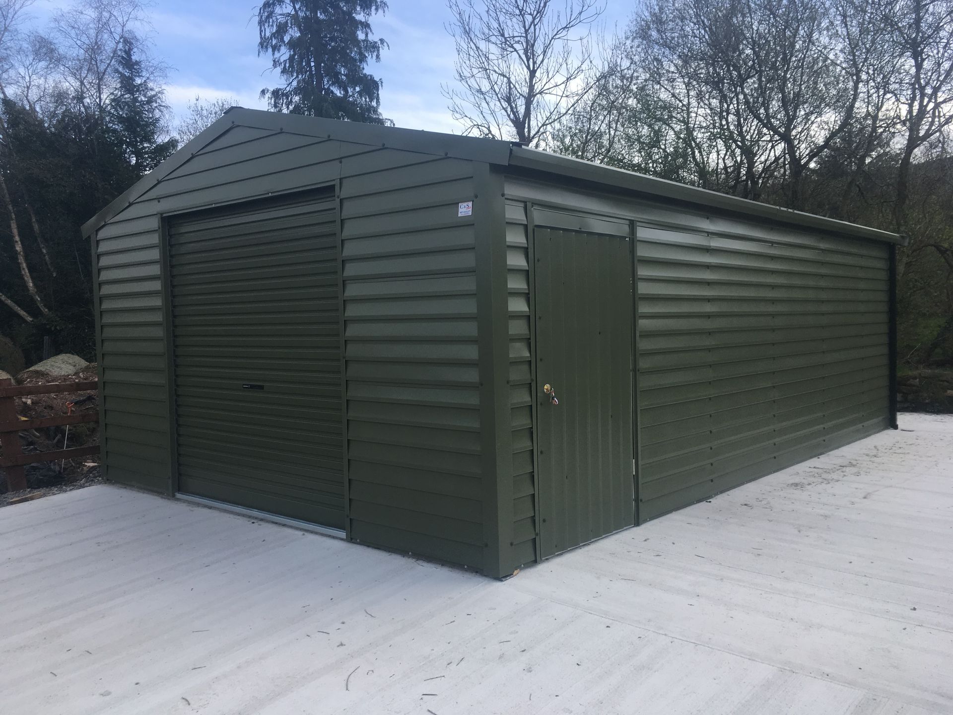 A green garage is sitting on top of a white concrete driveway.