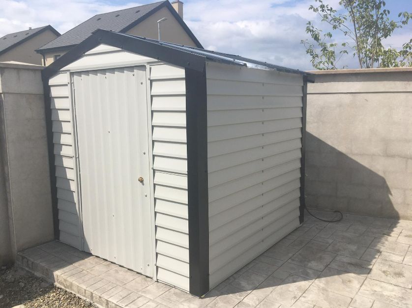 A white shed with a black trim sits next to a wall
