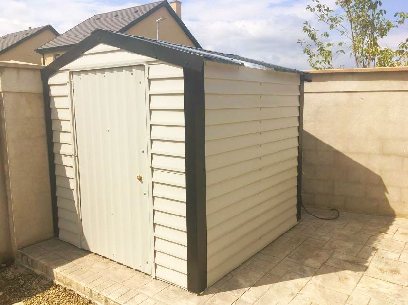 A white shed with a black trim sits in a backyard