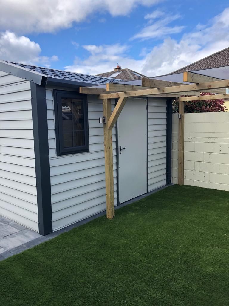 A white shed with a pergola attached to it in a backyard.