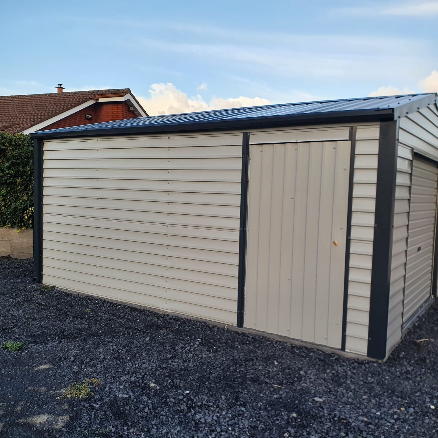 A white garage with a black trim is sitting in a gravel lot.