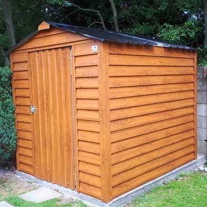 A wooden shed is sitting in the middle of a lush green yard.