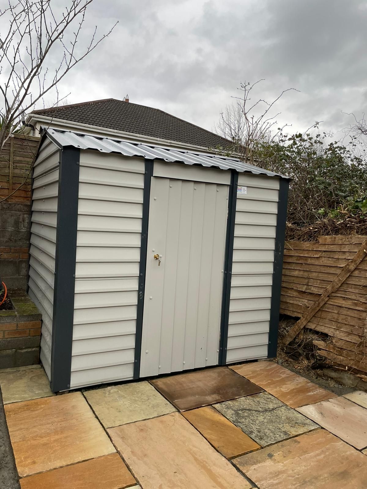 A white shed is sitting on a patio next to a house.